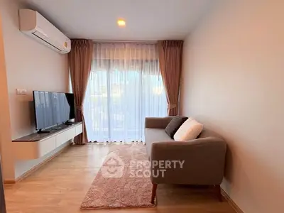 Cozy living room with modern sofa, TV, and natural light through large windows.