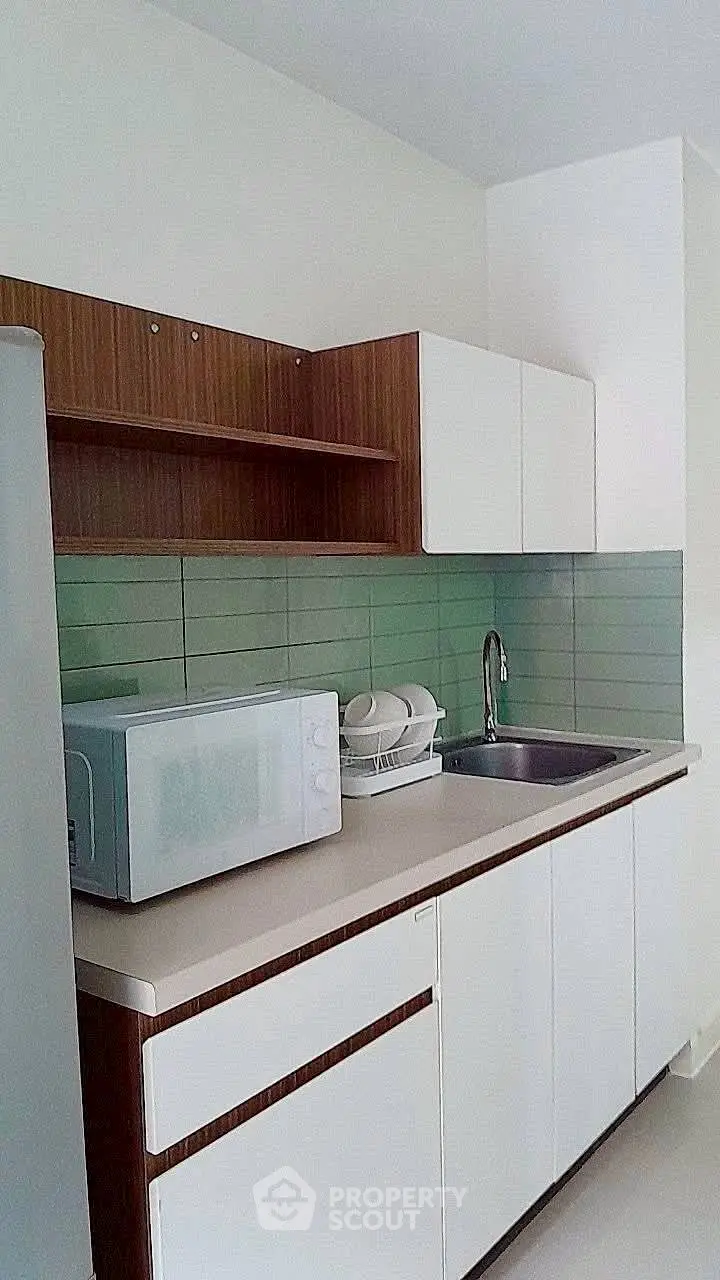 Modern kitchen with sleek cabinetry and green backsplash, featuring a microwave and sink.