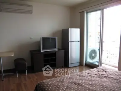 Cozy bedroom with TV and fridge, featuring balcony access and air conditioning.