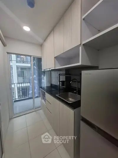Modern kitchen with sleek cabinetry and balcony view in urban apartment.