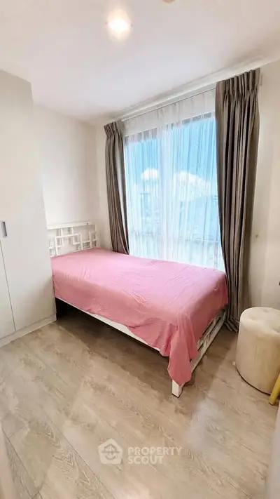 Cozy bedroom with single bed and large window, featuring elegant curtains and light wood flooring.