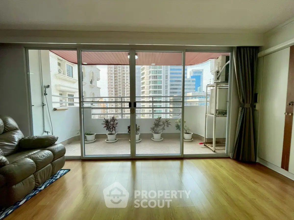 Spacious living room with large balcony and city view, featuring modern decor and wooden flooring.