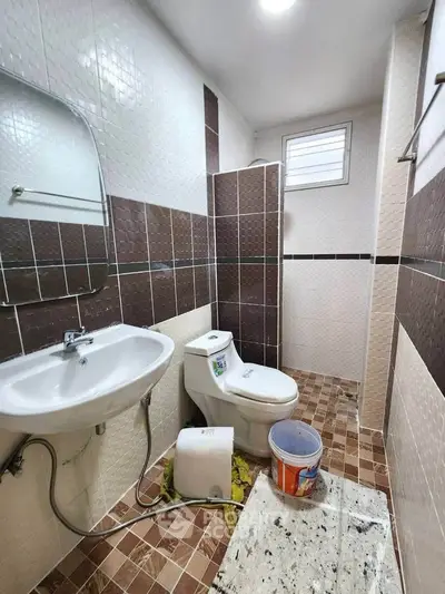 Compact bathroom with modern fixtures and tiled walls, featuring a sink, toilet, and small window for ventilation.