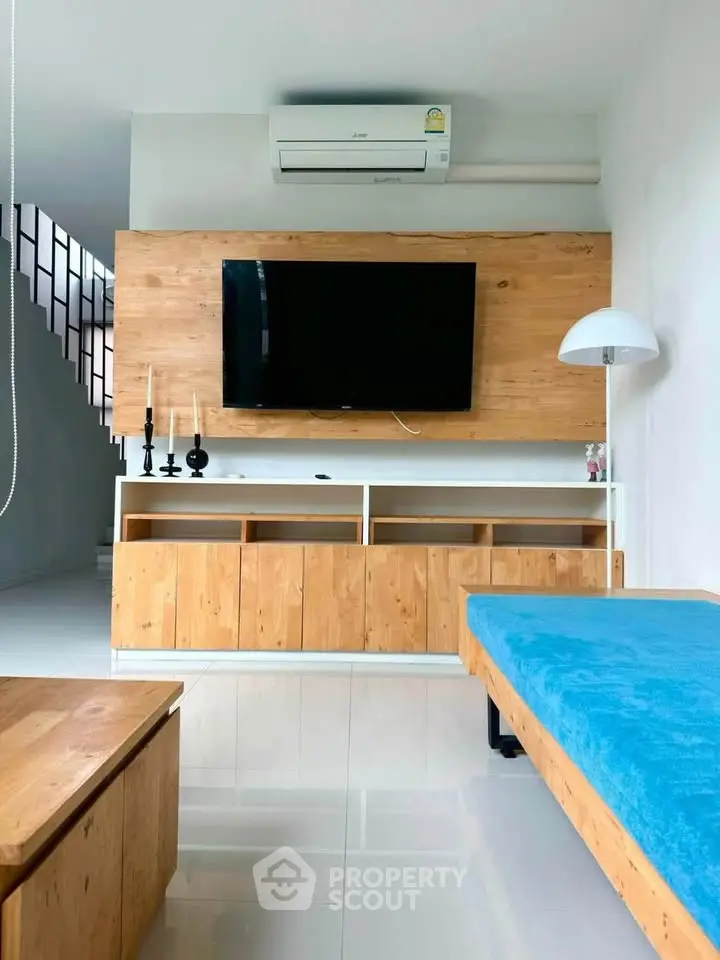 Modern living room with sleek wooden furniture and wall-mounted TV, featuring a cozy blue sofa and stylish decor.