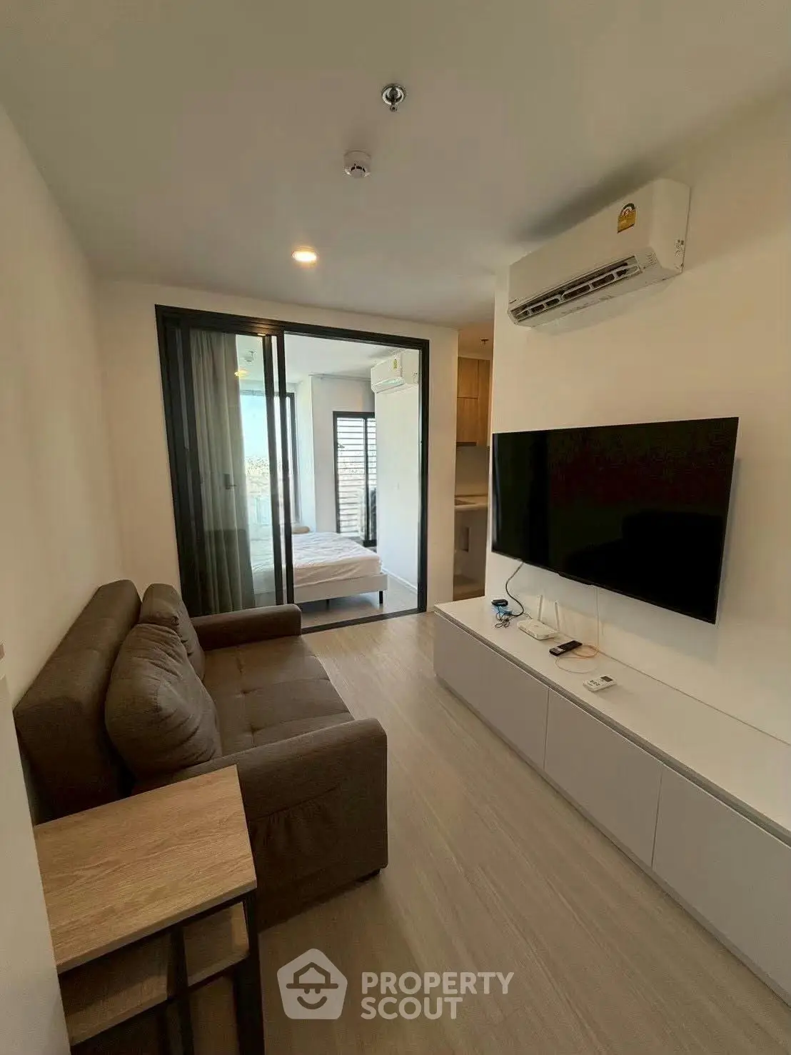 Modern living room with sleek design and large TV, adjacent to a cozy bedroom.