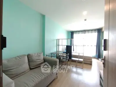 Modern living room with light teal walls, cozy sofa, and natural light from large window.