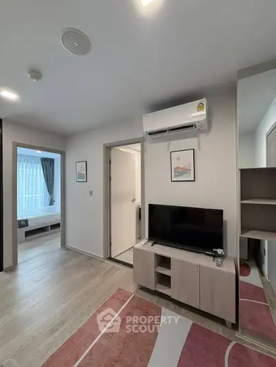 Modern living room with TV and air conditioning, leading to a cozy bedroom.