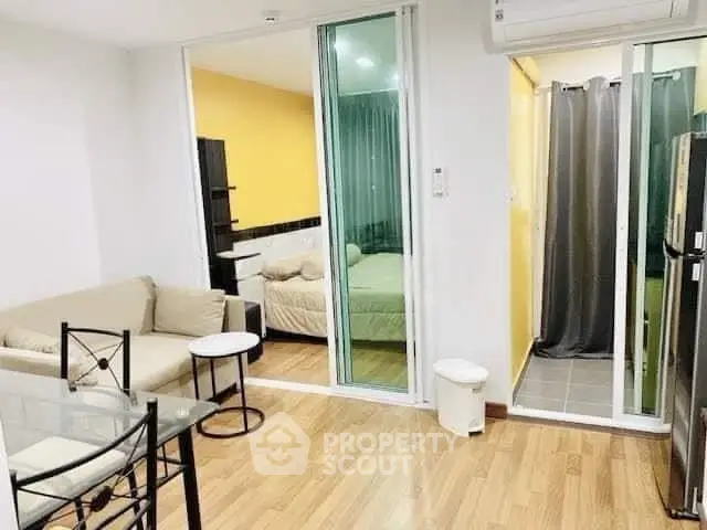 Modern apartment with open living room and bedroom, featuring sleek furniture and wooden flooring.