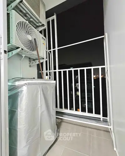 Compact balcony with air conditioning unit and city view at night.