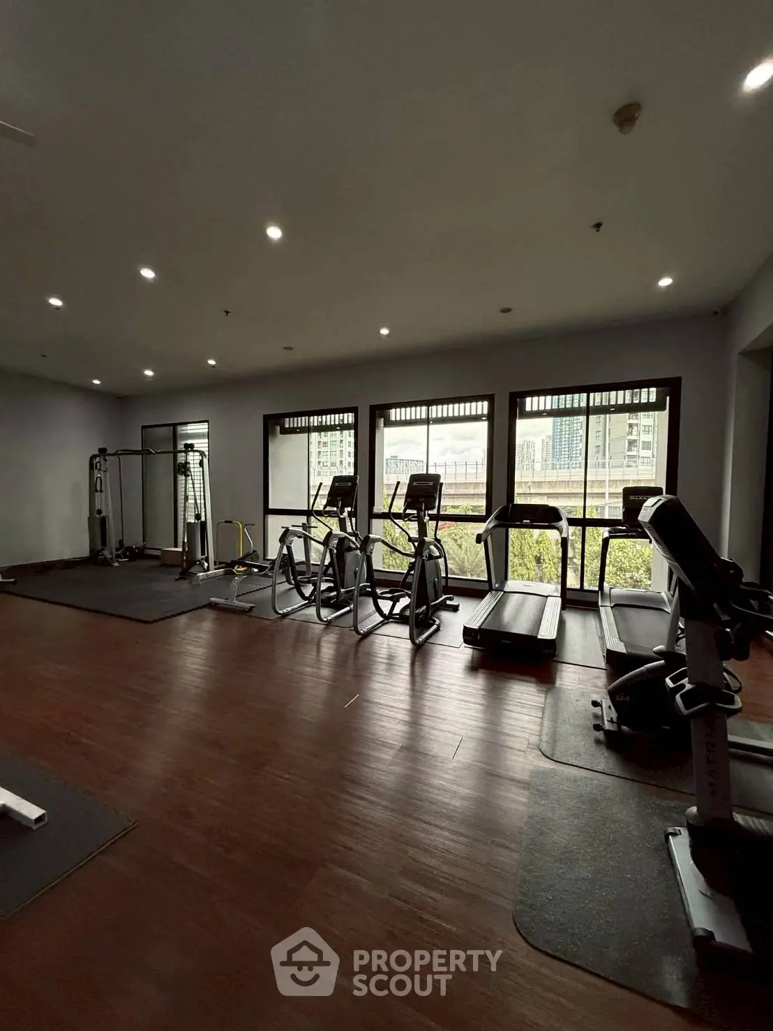 Spacious gym with modern equipment and large windows offering a city view, perfect for fitness enthusiasts.
