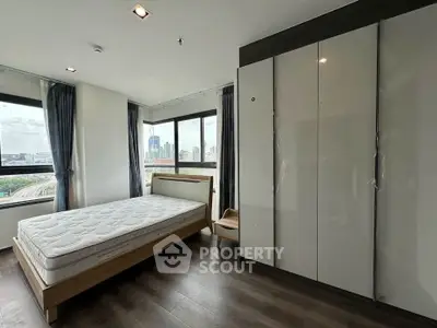 Modern bedroom with large windows and city view, featuring sleek wardrobe and wooden flooring.