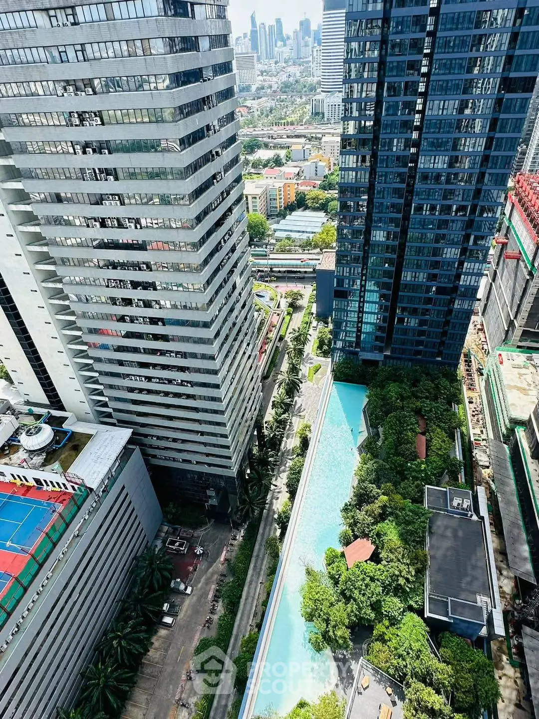 Stunning aerial view of modern high-rise buildings with lush greenery and a sleek swimming pool in an urban setting.