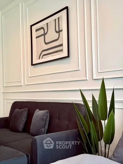 Elegant living room with modern art and stylish decor, featuring a sleek gray sofa and lush green plant.