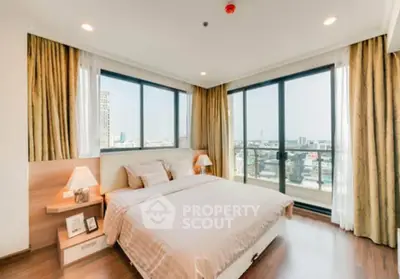 Spacious bedroom with large windows and city view, featuring elegant decor and natural light.