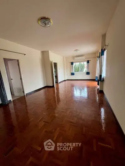 Spacious empty living room with polished wooden floors and large windows.