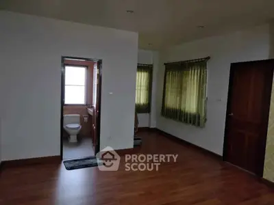 Spacious room with wooden flooring and attached bathroom, featuring large windows with green curtains.