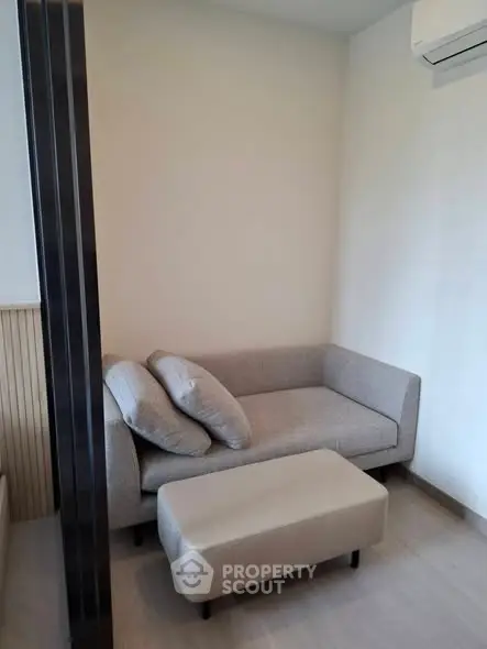 Cozy modern living room with stylish sofa and ottoman, featuring minimalist design and air conditioning.