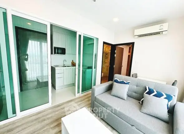 Modern living room with glass partition and compact kitchen in stylish apartment.