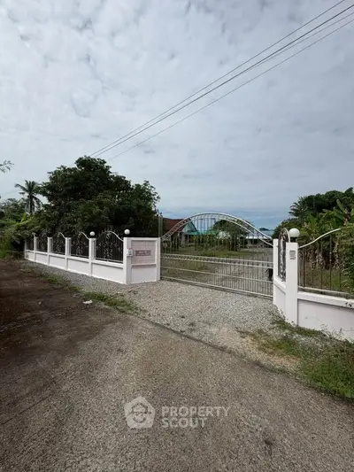 Charming gated property entrance with lush greenery and spacious driveway.