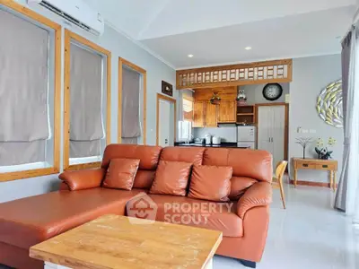 Spacious living room with modern kitchen in open layout, featuring stylish leather sofa and wooden accents.