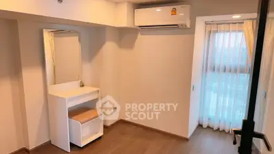Cozy bedroom with air conditioning and natural light, featuring a stylish vanity and wooden flooring.