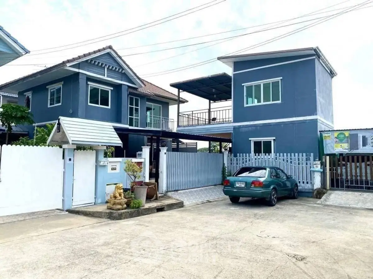 Charming blue two-story house with spacious driveway and carport in a serene neighborhood.
