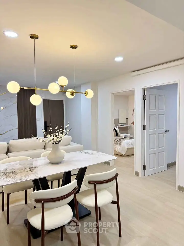 Modern open-plan living and dining area with elegant lighting and cozy bedroom view.