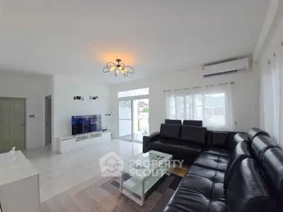 Spacious modern living room with sleek black leather sofa and large TV, perfect for relaxation.