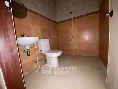 Spacious bathroom with tiled walls and floor, featuring a toilet and sink, ideal for modern living.