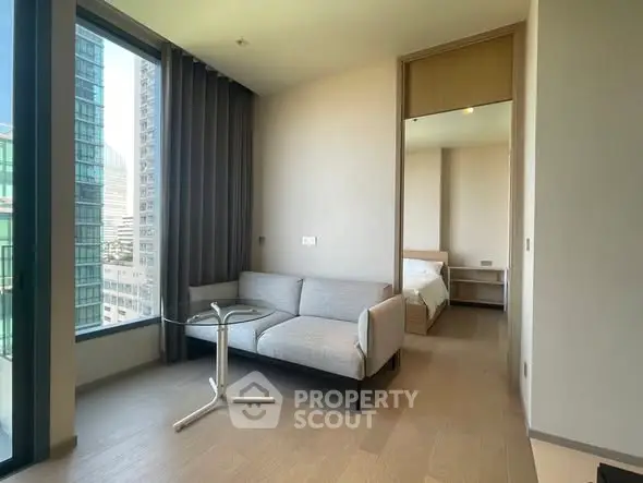 Modern apartment with a cozy living room and bedroom view, featuring large windows and sleek furniture.