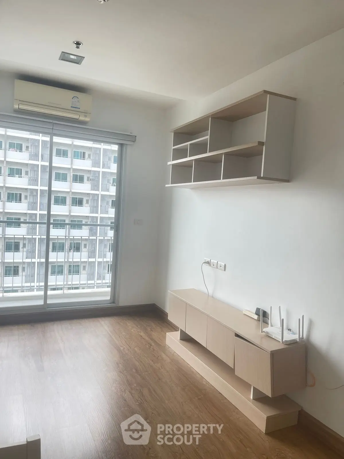 Modern living room with wooden flooring and built-in shelves, featuring a large window with city view.