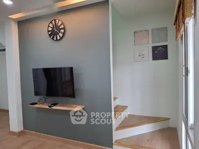 Modern living room with stylish wall clock and mounted TV, featuring wooden staircase and elegant decor.