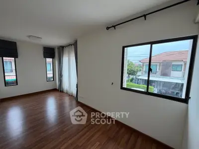Spacious empty room with large windows and wooden flooring in modern home
