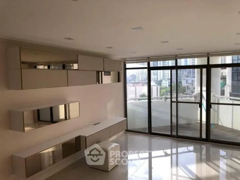 Spacious modern living room with large windows and city view, featuring sleek storage units and glossy flooring.