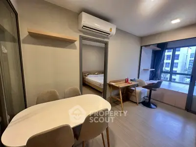 Modern apartment interior with dining area and bedroom view, featuring sleek furniture and natural light.