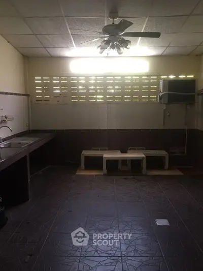 Spacious kitchen with tiled floor and ceiling fan, featuring a large sink and ample natural light.