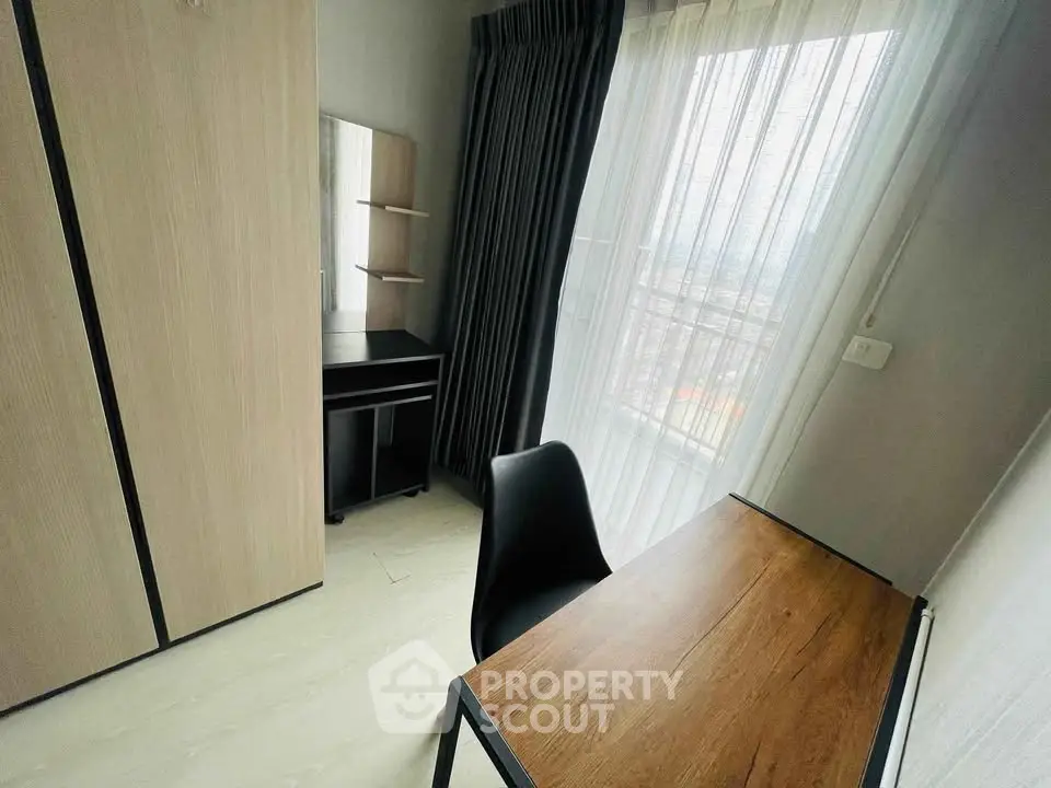 Cozy study room with wooden desk and wardrobe, featuring large window with city view.
