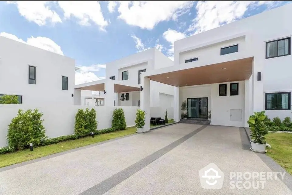 Modern white minimalist house with spacious driveway and lush greenery