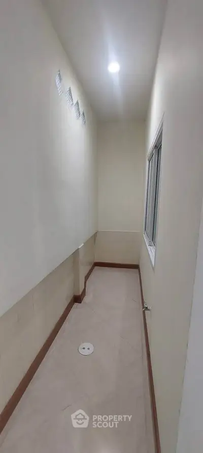 Narrow utility room with tiled floor and window, ideal for storage or laundry setup.