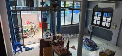 Spacious living room with large windows and ceiling fan, overlooking a patio with bicycle and storage items.