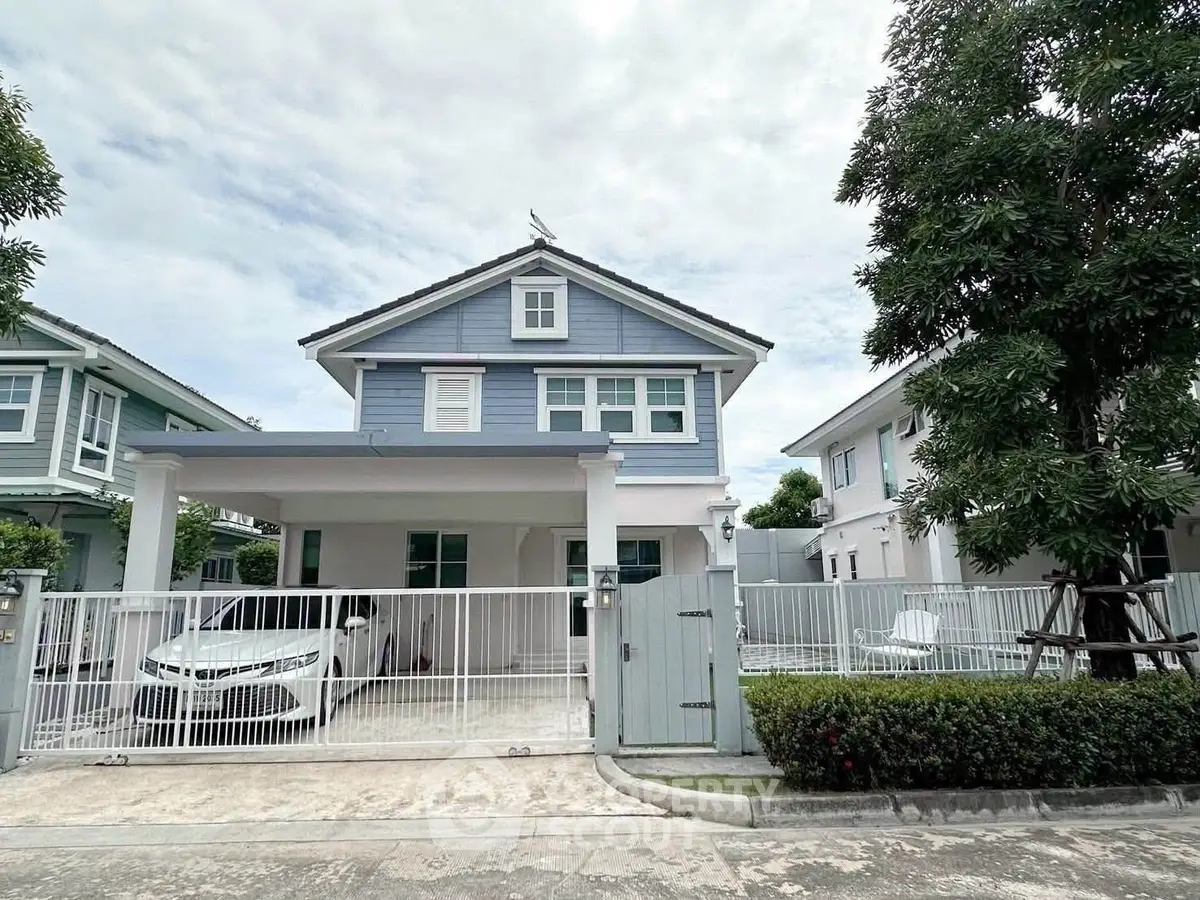 Charming two-story blue house with a gated driveway and lush greenery, perfect for family living.