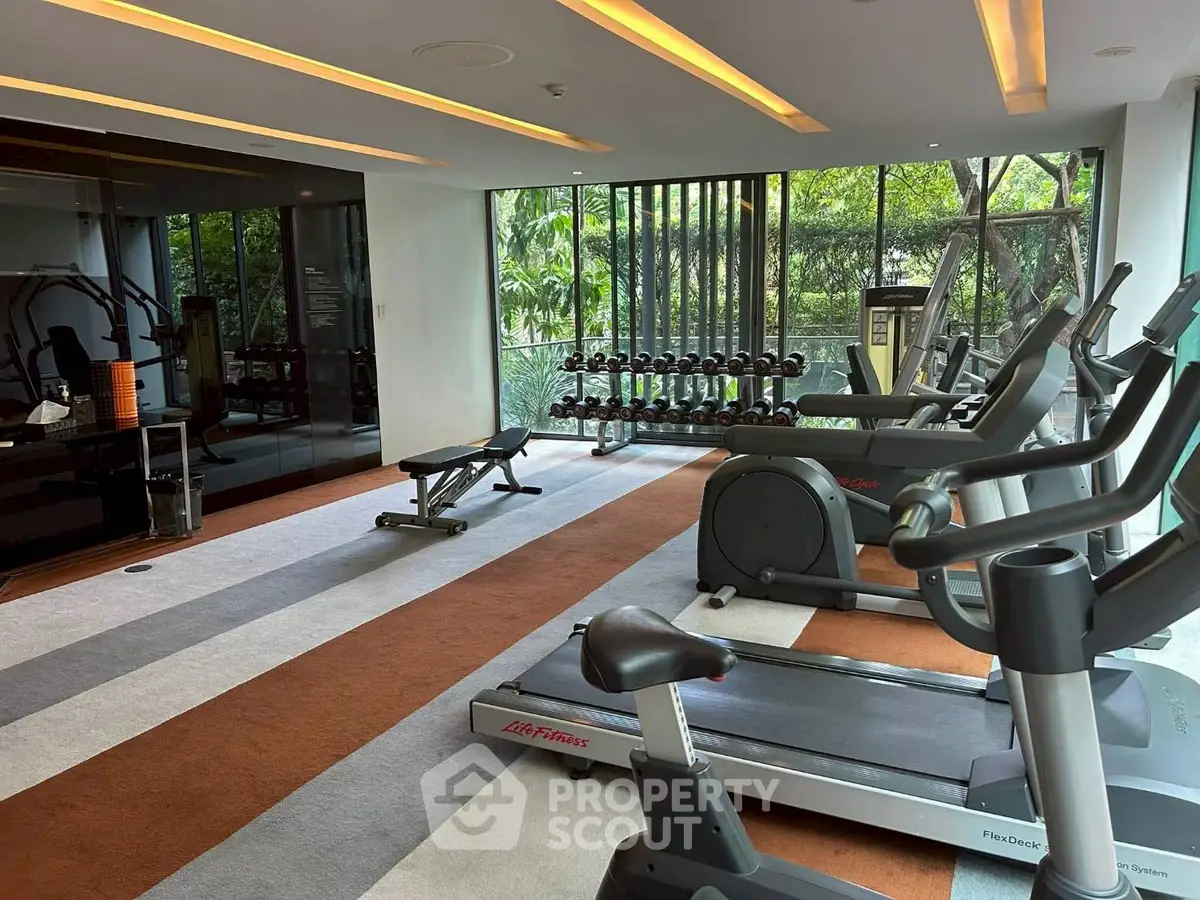 Modern gym with state-of-the-art equipment and lush garden views, perfect for fitness enthusiasts.