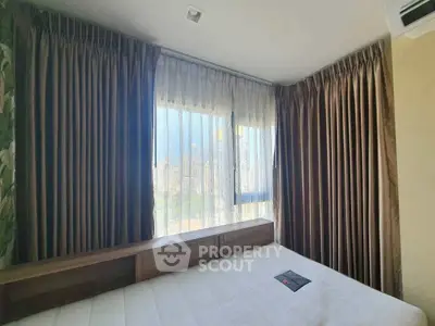Cozy bedroom with large window offering city view and elegant curtains.