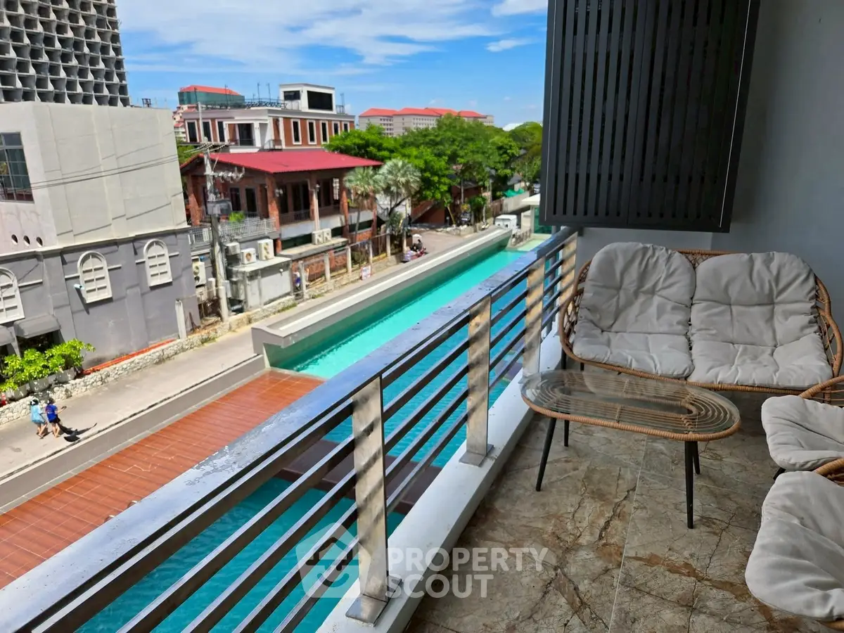 Charming balcony with cozy seating overlooking a vibrant cityscape and pool.