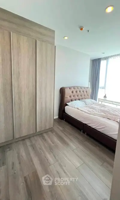 Spacious bedroom with elegant bed and large wardrobe, featuring natural light from a big window.