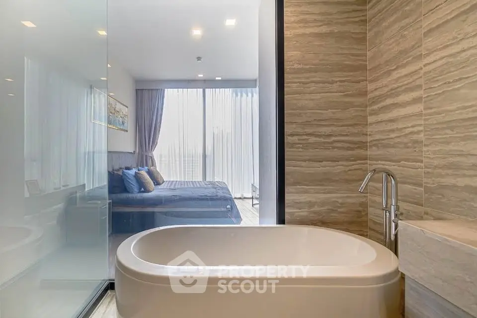 Luxurious modern bathroom with freestanding bathtub and view into elegant bedroom.