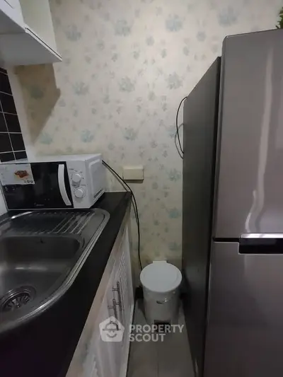 Compact kitchen with fridge, microwave, and sink in cozy apartment.