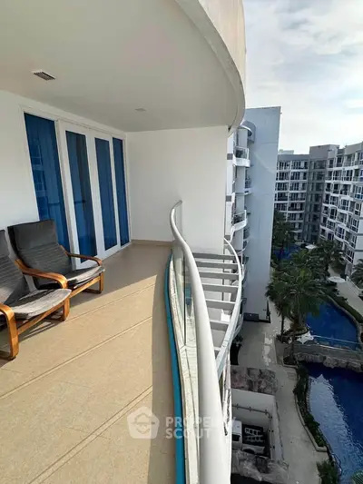 Spacious balcony with modern chairs overlooking pool and garden in luxury apartment complex.