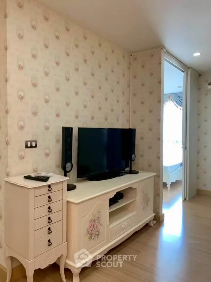 Charming living room with vintage decor and modern TV setup, leading to a cozy bedroom.