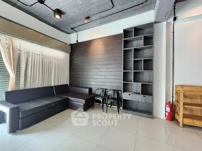 Modern living room with sleek black sofa and built-in shelving, featuring industrial ceiling design.